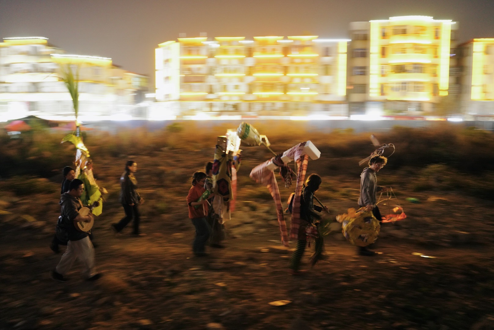 Group of young artists walking through urban wasteland carrying colourful puppets